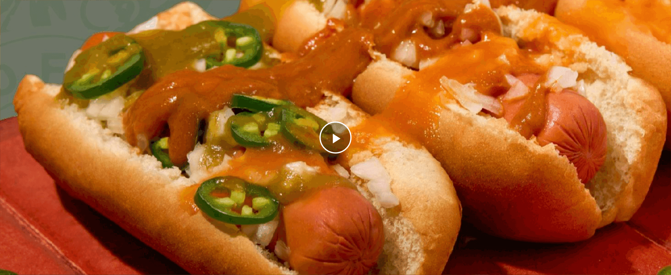 Shows the loaded hot dogs in an appetizing close-up to invite shoppers to play a video demonstrating the sauce in use.