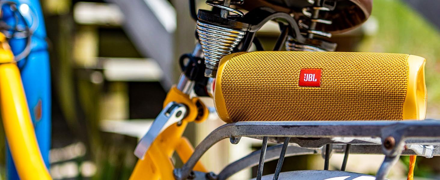 Shows the yellow JBL speaker resting on a bicycle rack in an outdoor setting to help shoppers envision taking it along on adventures.
