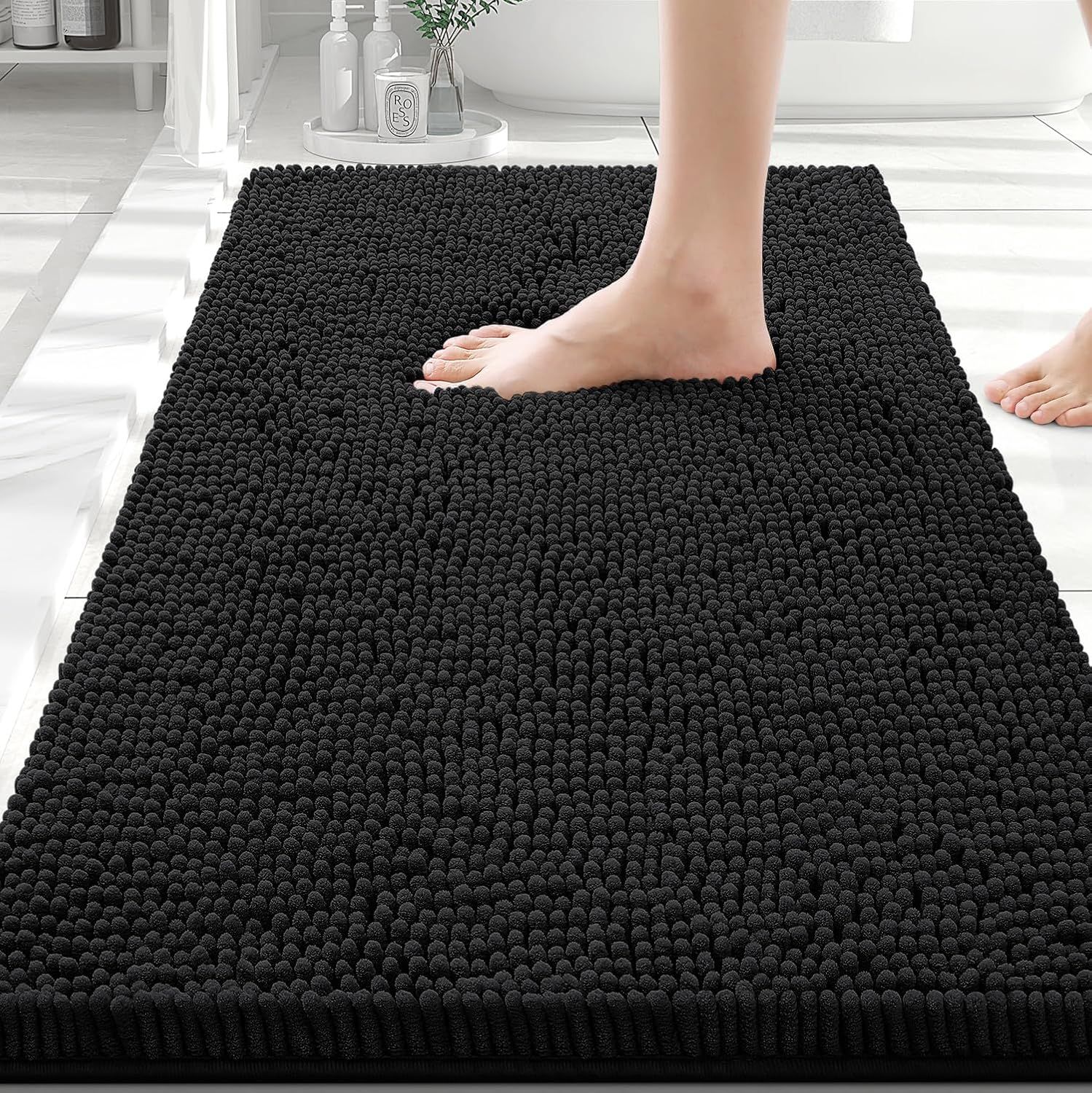 Shows a person standing on the bath mat to demonstrate its size, plush texture, and comfort underfoot, helping shoppers visualize how it will feel and fit in their bathroom. Displays the bath mat in…
