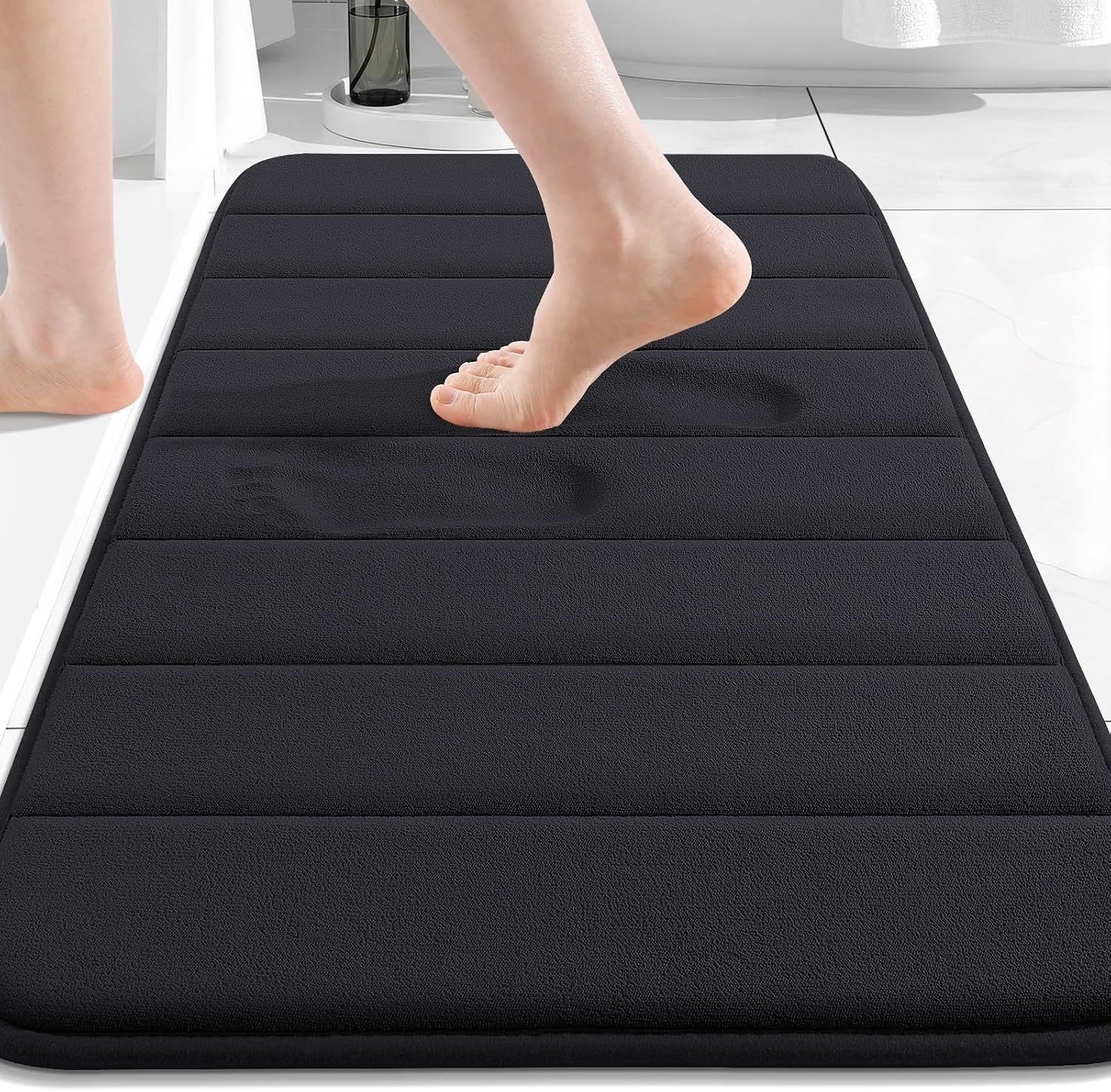 Shows the core product, a black memory foam bath mat with horizontal ribbed texture, displayed in a bathroom setting to help shoppers visualize the product. Demonstrates the mat's memory foam…