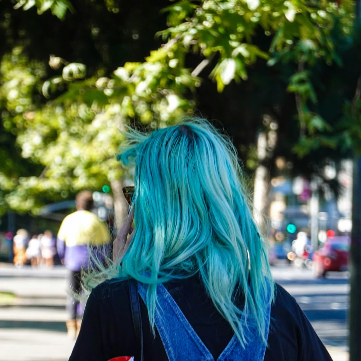 Shows a person with bright blue hair in an outdoor setting, suggesting the product creates bold, eye-catching hair color results.