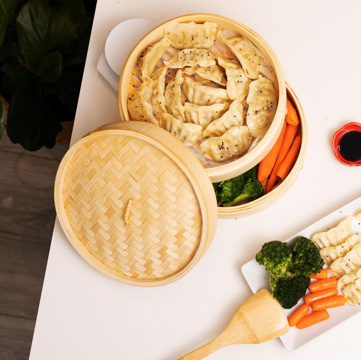 Shows the product in use, presenting steamed dumplings in a bamboo steamer alongside vegetables, demonstrating how the product is used in a real-world dining context.