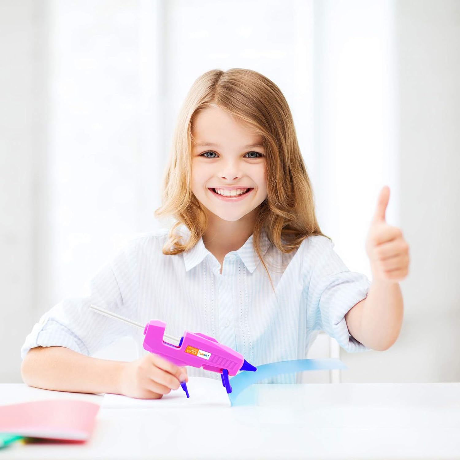 Shows a young girl happily using the product, likely a glue gun, to demonstrate its ease of use and suitability for children's crafts.