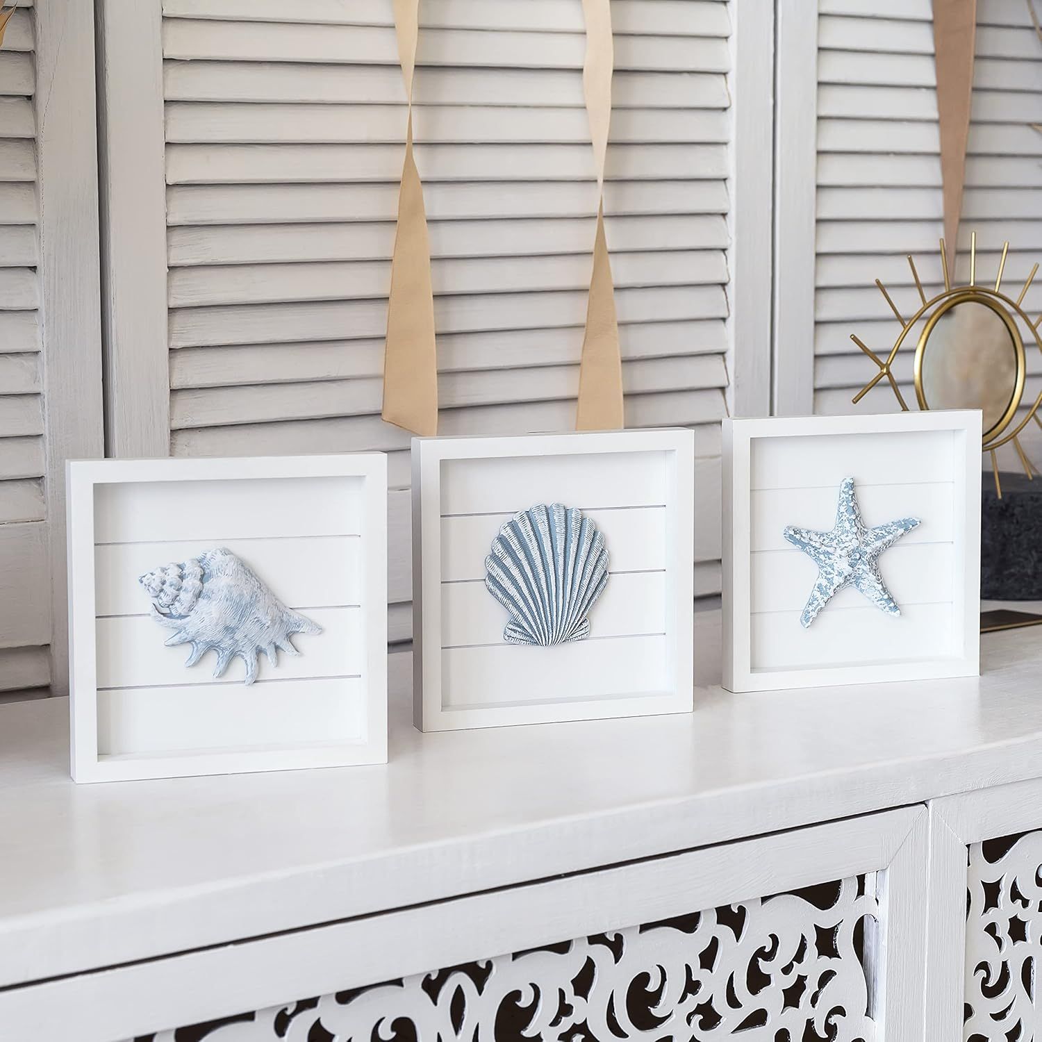 Shows the product in a real-world home setting to help shoppers visualize how the framed coastal art pieces would look styled on a shelf or mantle in their own space.