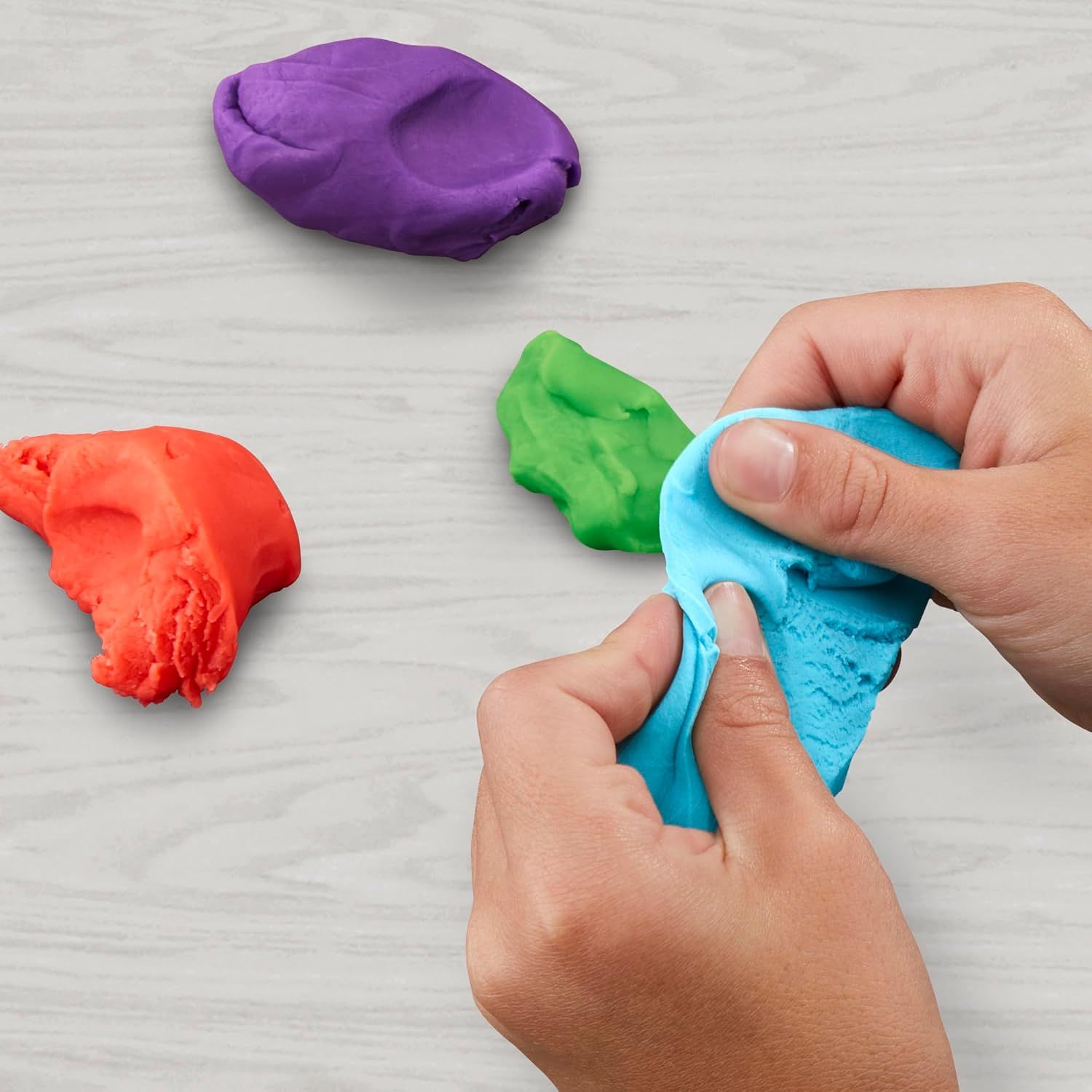 Demonstrates the product in use within a real-world play context, showing hands actively manipulating the colorful play dough to convey its tactile, sensory…