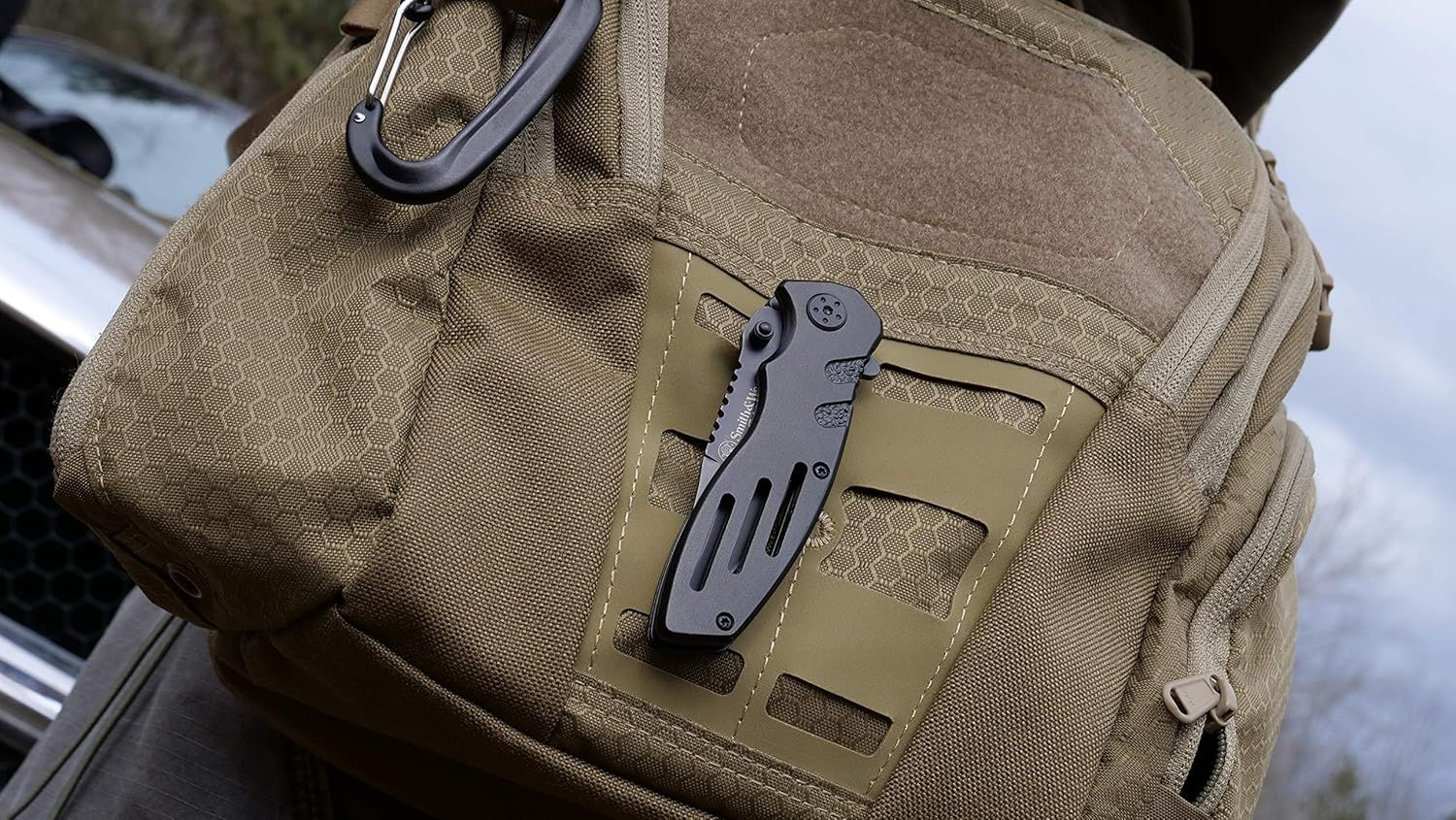 Demonstrates the product in a real-world tactical/outdoor context, showing how the multi-tool knife can be conveniently attached to gear via carabiner for…