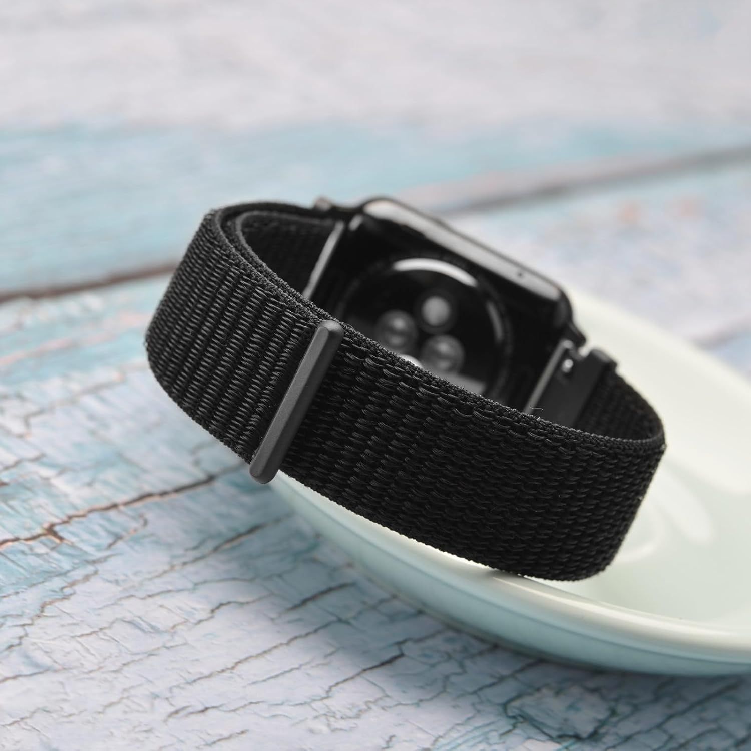 Displays the smartwatch with its black woven band in a clean, lifestyle setting to showcase the product's design and style without distractions.