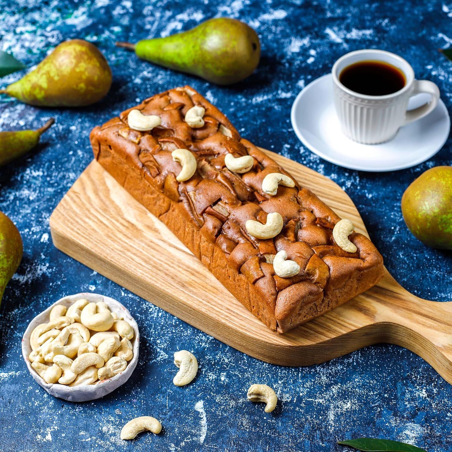 Showcases the product (loaf cake) in an appealing, aspirational lifestyle setting with complementary items like coffee, fresh pears, and cashews to evoke a…