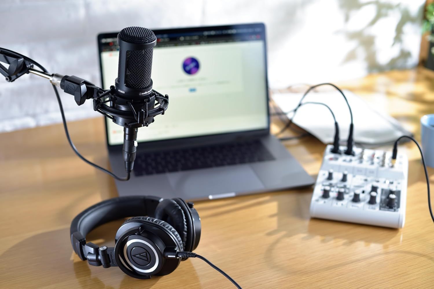 Demonstrates the product in a real-world professional audio recording or streaming context, showing how it integrates into a complete setup with laptop, headphones, and audio interface.