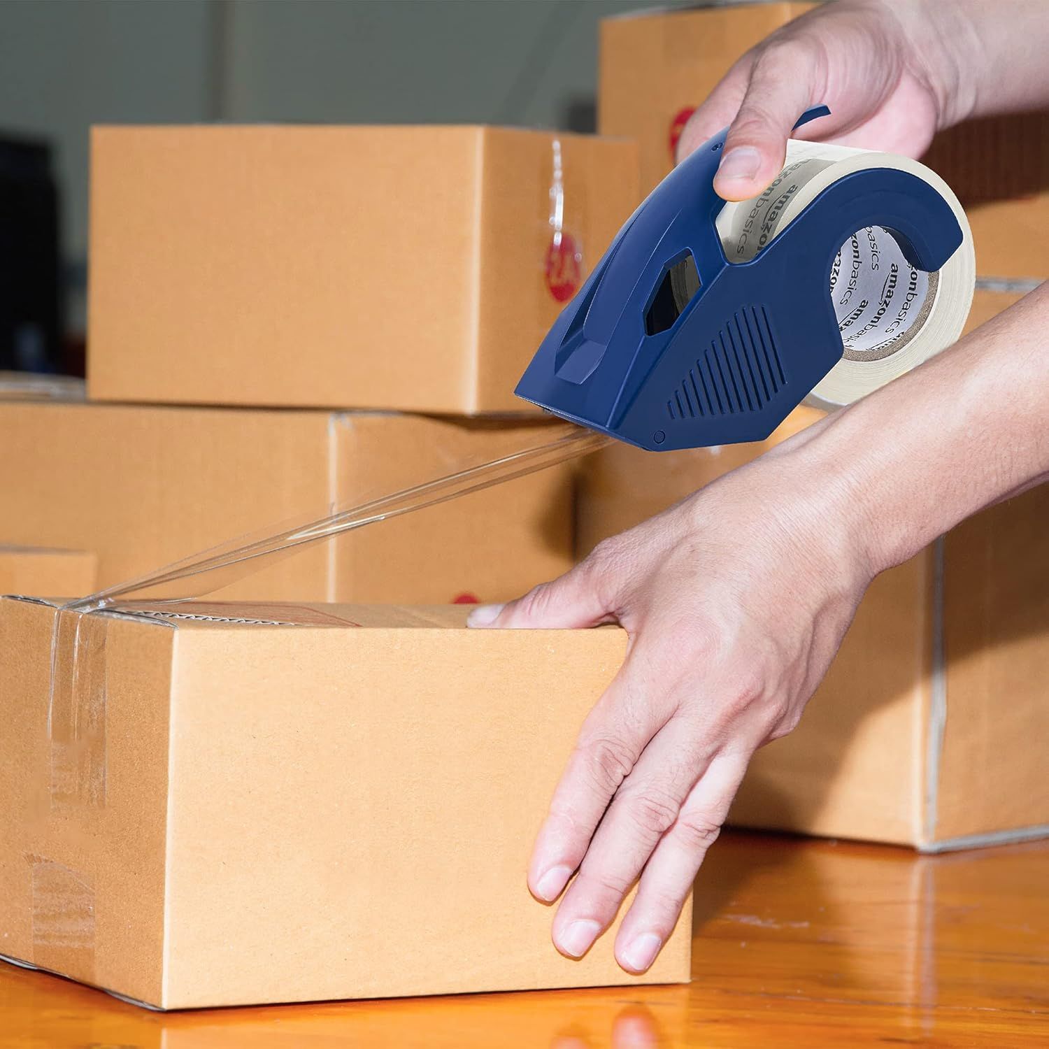 Demonstrates the product in a real-world context, showing someone using the tape dispenser to seal cardboard boxes, helping shoppers visualize practical…
