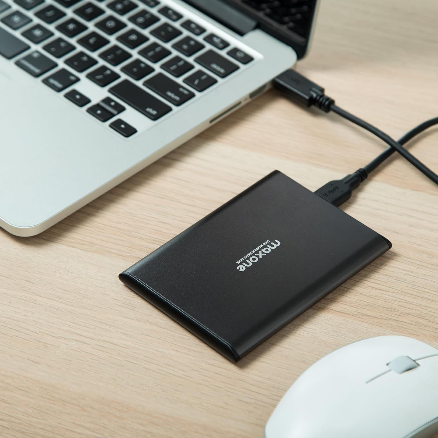 Shows the external hard drive in a real-world office environment connected to a laptop, helping shoppers visualize how the product fits into their daily workflow.