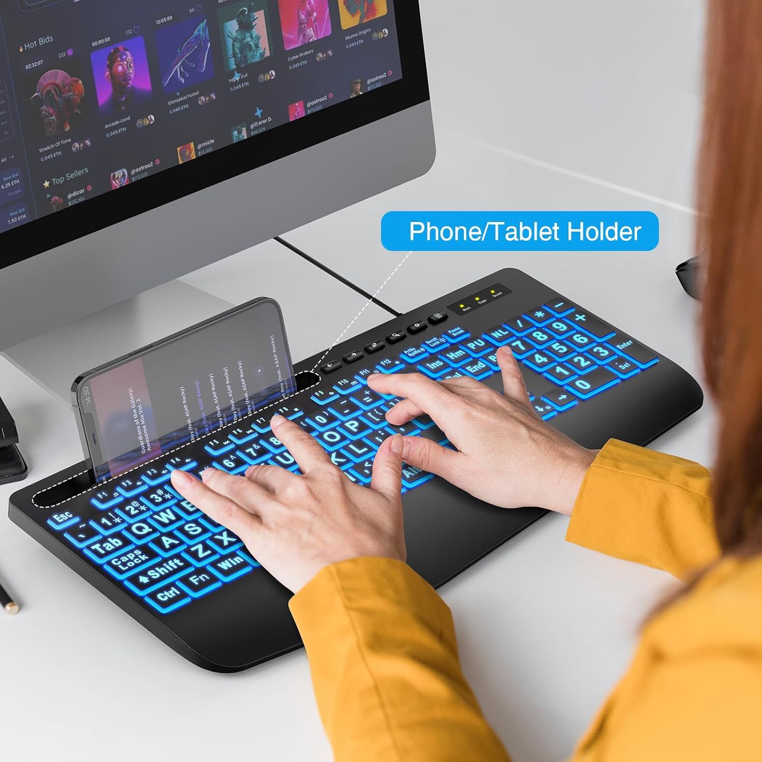 Demonstrates the keyboard's built-in phone/tablet holder feature, showing how users can conveniently position their mobile device while typing for improved multitasking and ergonomics.