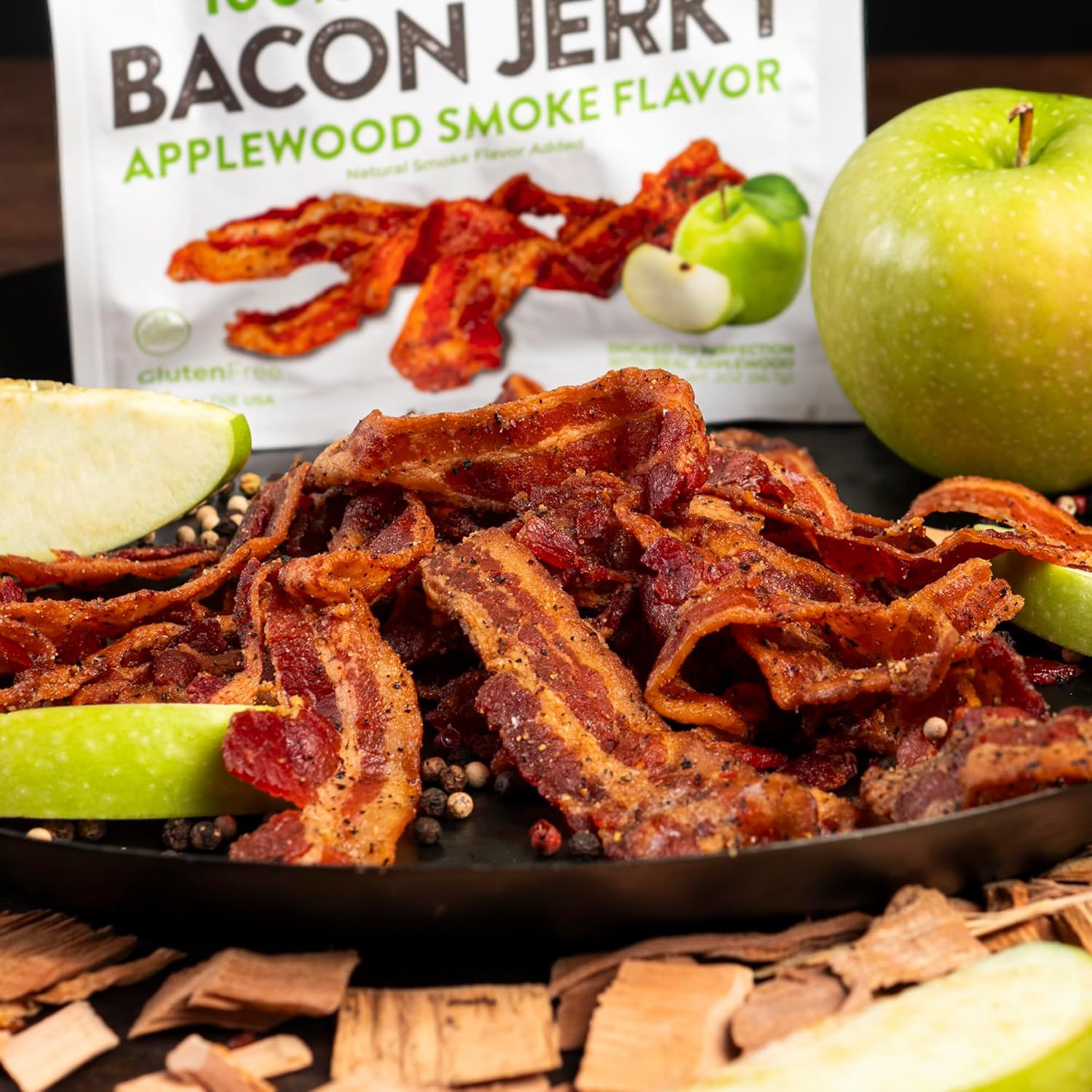 Showcases the bacon jerky product in an appetizing, real-world serving context with fresh apples and peppercorns to help shoppers visualize how they might enjoy the product.