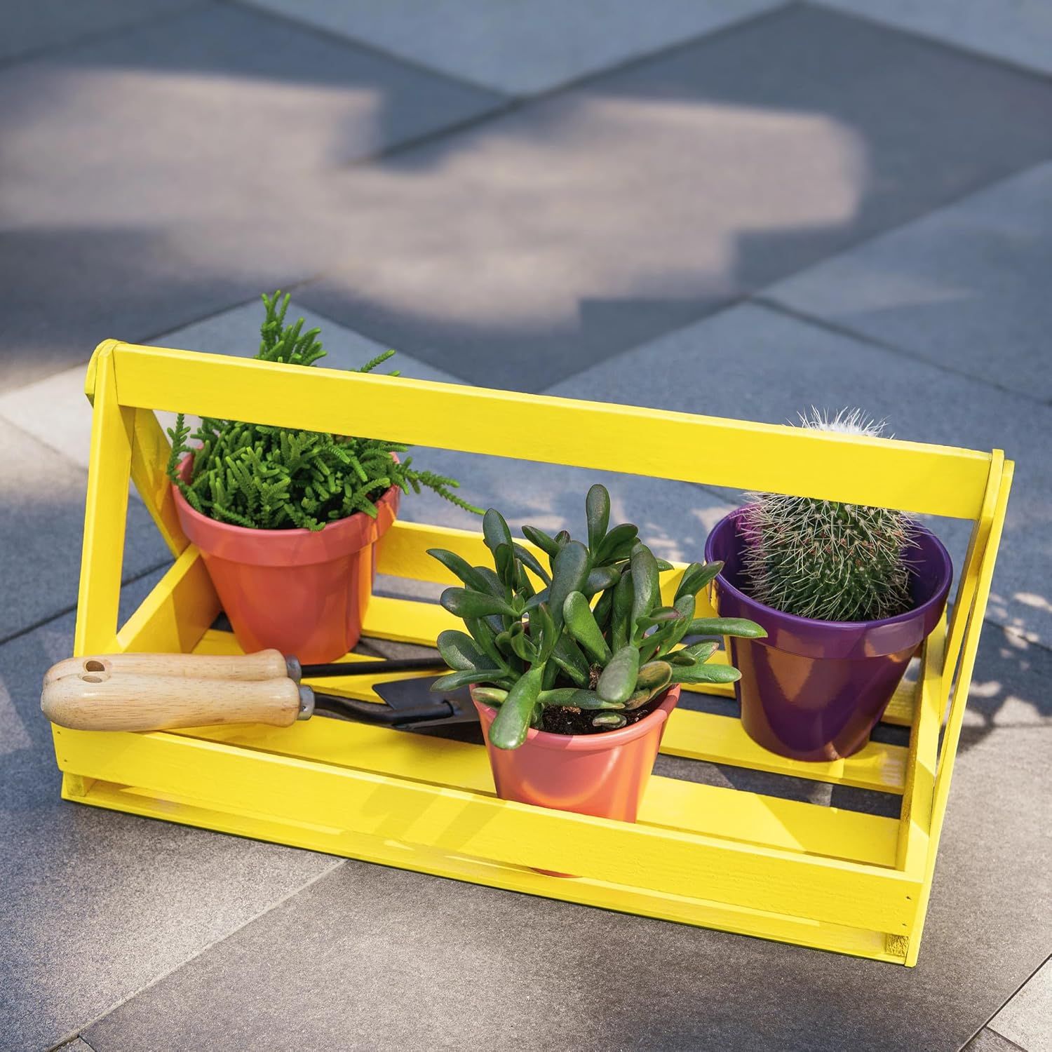 Demonstrates the product in a real-world outdoor setting with plants and gardening tools to show how it can be used for organizing and displaying small potted plants.