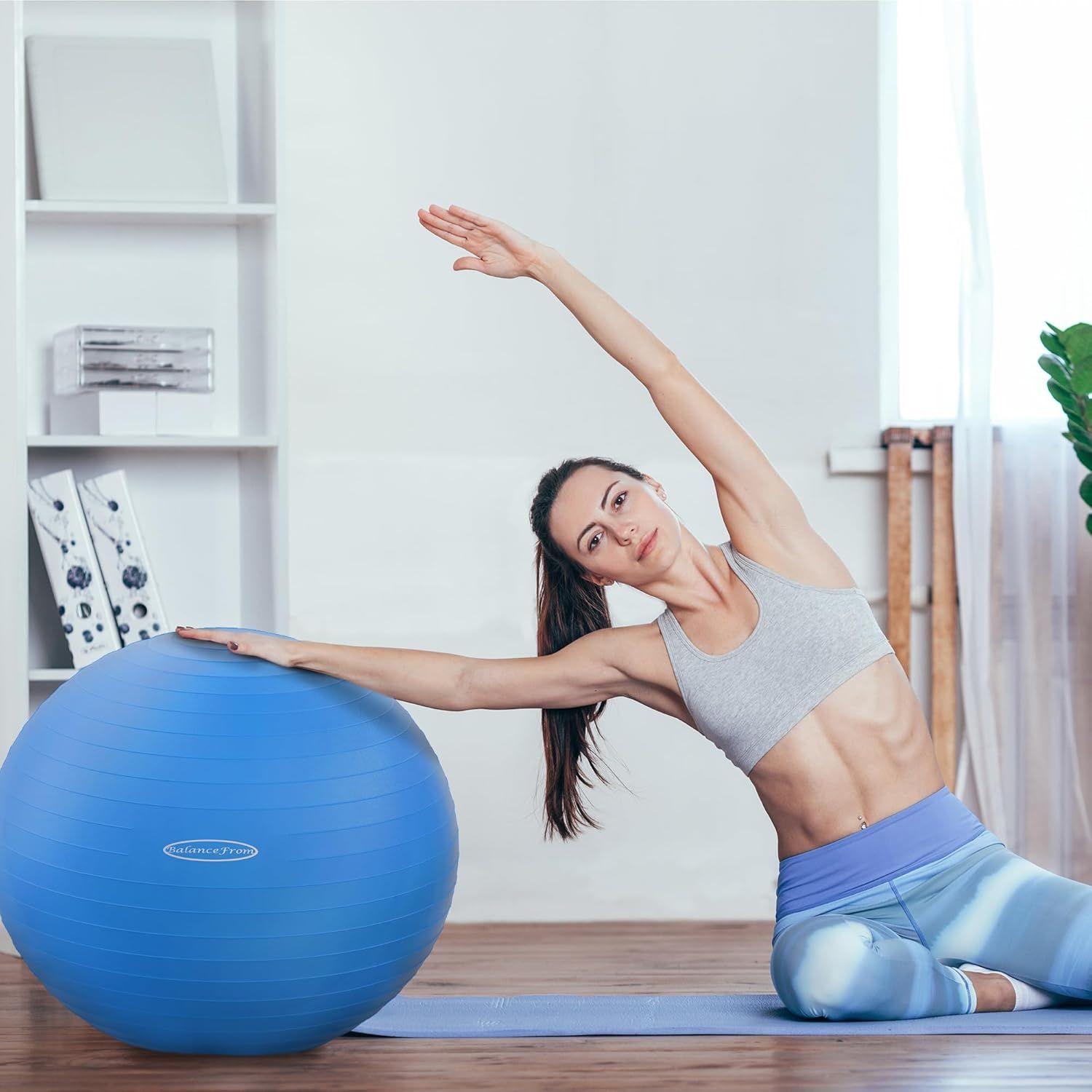 Demonstrates the product (exercise ball) being used in a real-world home fitness setting to help shoppers visualize how they would use it in their own space.