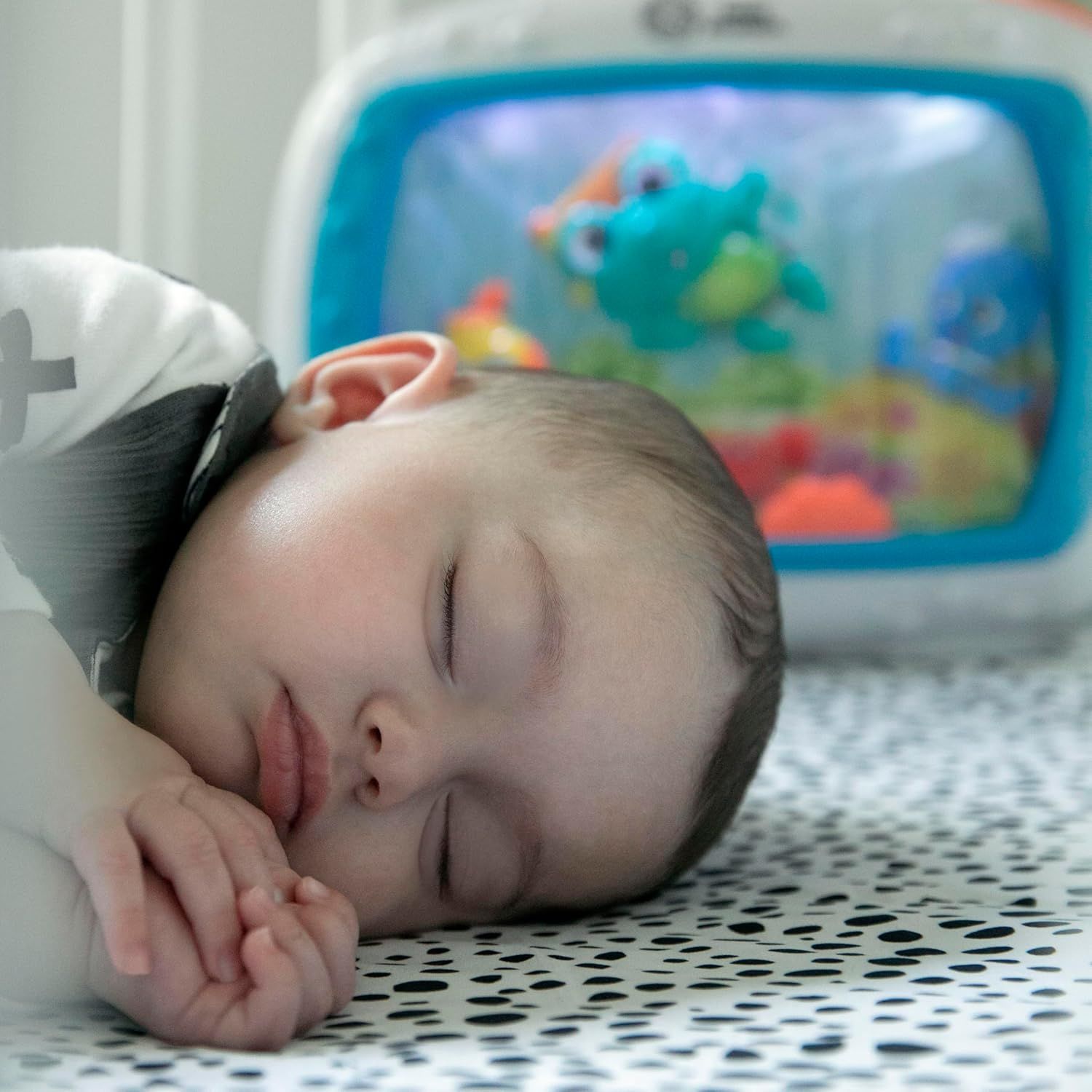 Shows the product in a natural home setting with a baby sleeping peacefully nearby, demonstrating the product's gentle, non-disruptive nature and suitability for use around infants.