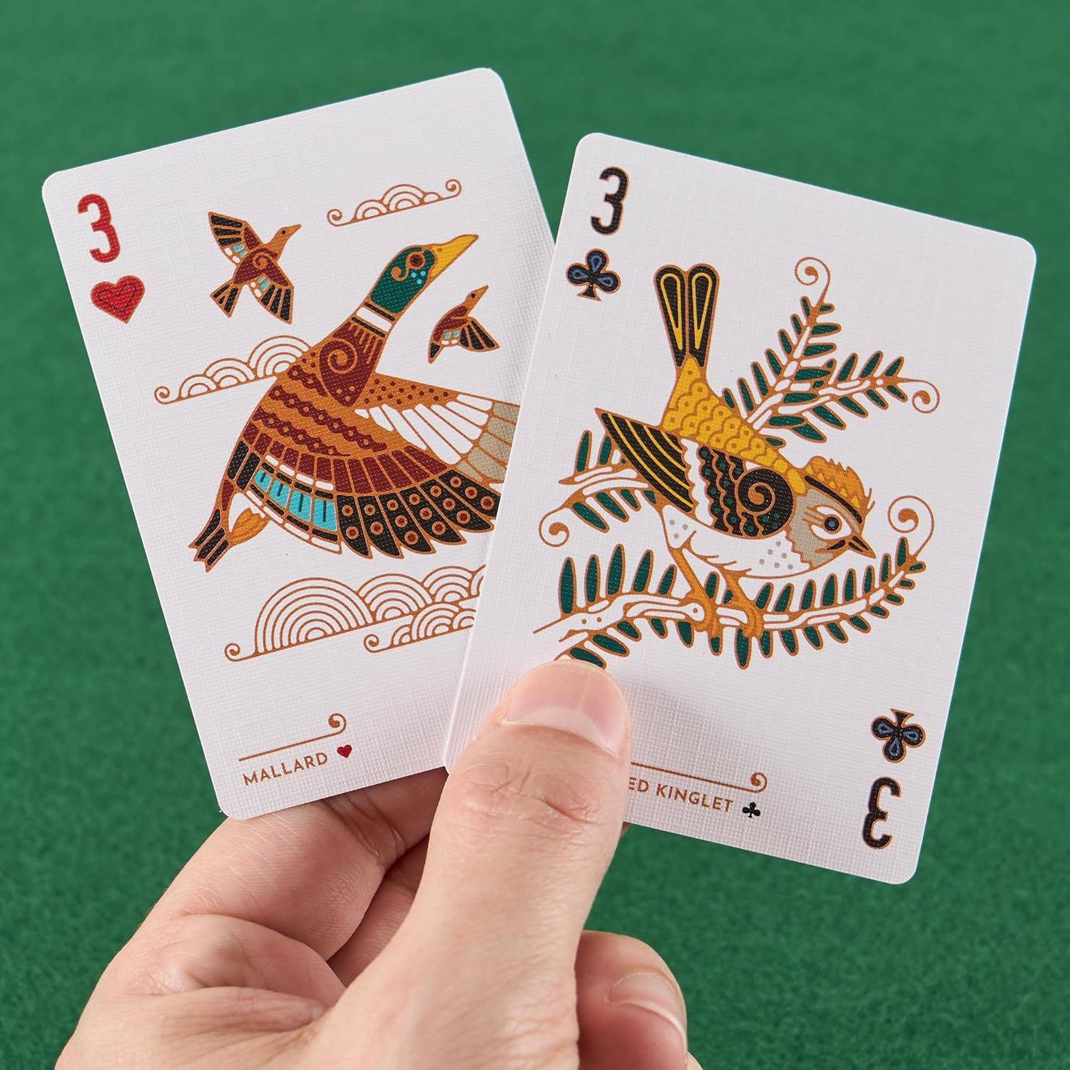 Shows the artistic design and quality of the playing cards included in the deck, highlighting the unique decorative artwork featuring birds (mallard and kinglet) to communicate the premium aesthetic…