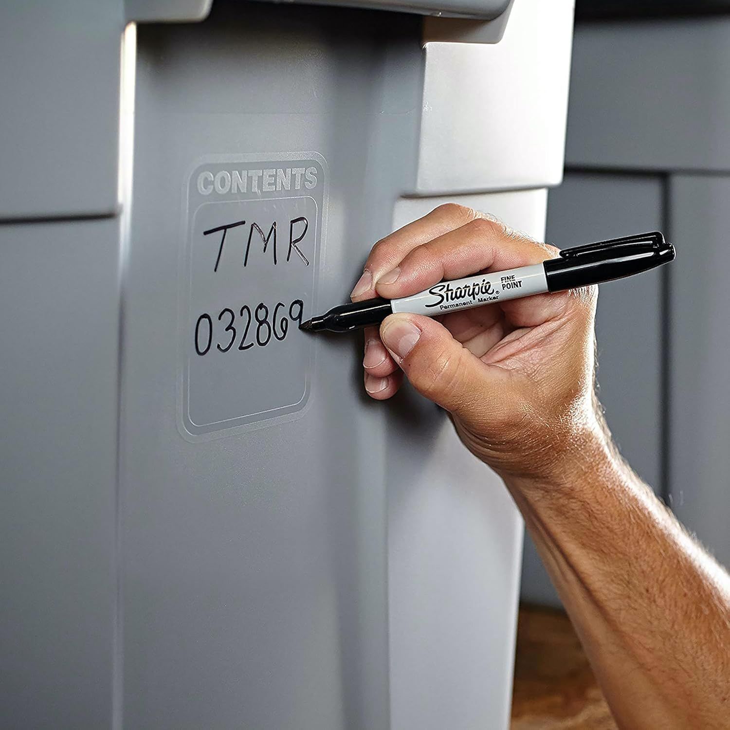 Demonstrates the product in a practical, real-world context showing someone using the Sharpie marker to label a storage bin, emphasizing its everyday utility for organization and identification…