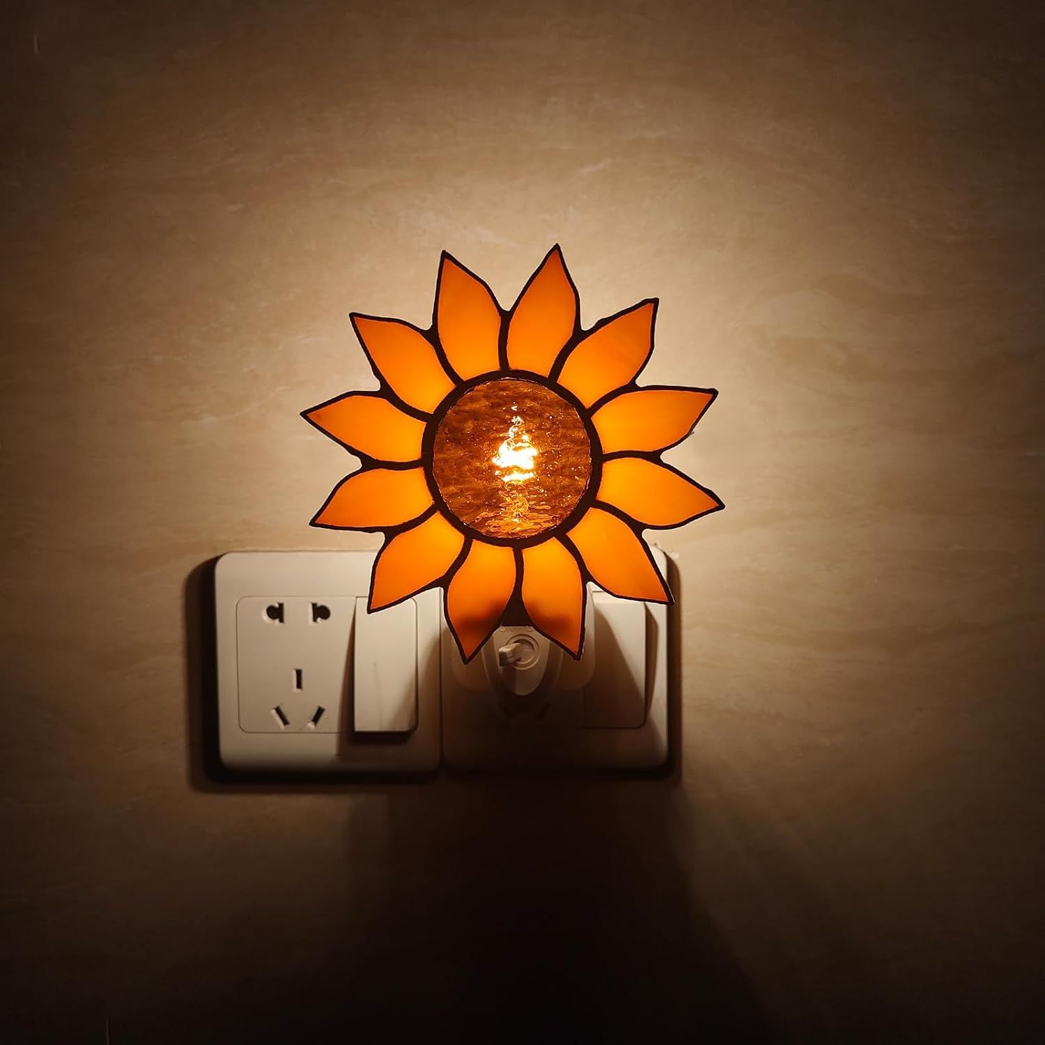 Displays the night light illuminated and plugged into a wall outlet in a real-world setting to show how it looks when in use.
