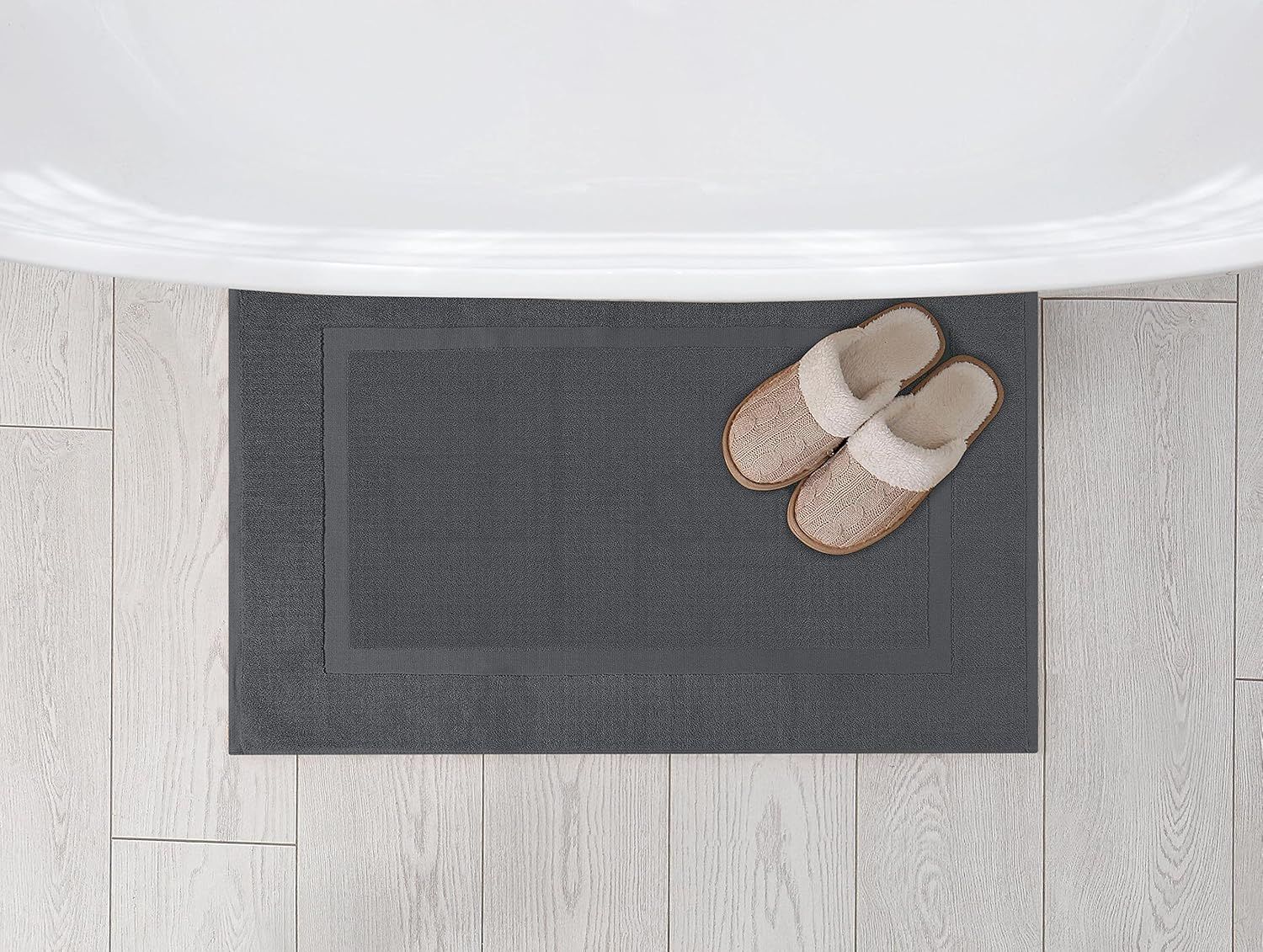 Displays the bath mat from an overhead perspective in a home setting with slippers, showing its size and how it fits in a real space.