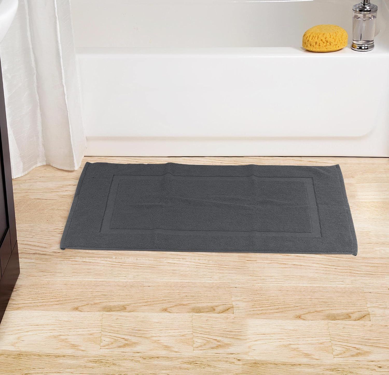 Displays the bath mat positioned in a bathroom setting near a tub, showing its intended placement and how it complements bathroom decor.