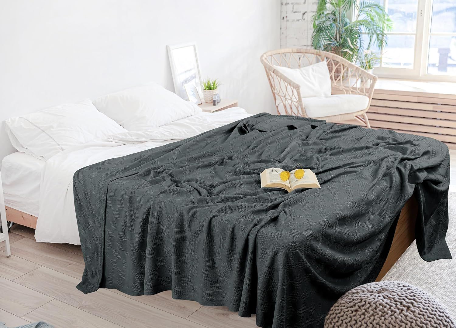 Shows the blanket draped over a bed in a bright, airy bedroom setting with a book on top, conveying a relaxing lifestyle moment without any text overlay.