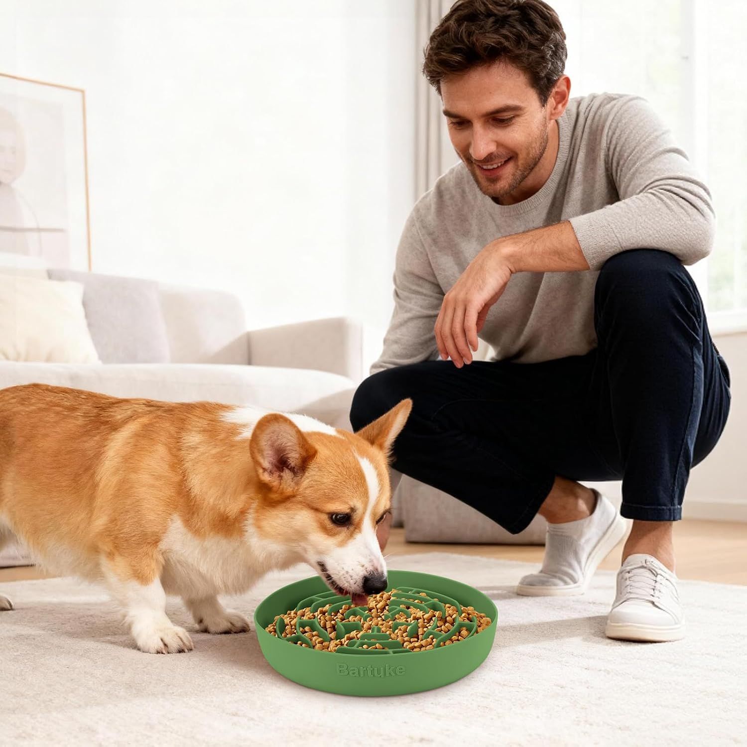 Shows the product in a real-world home setting with a dog eating from the bowl while the owner watches, demonstrating natural usage context.