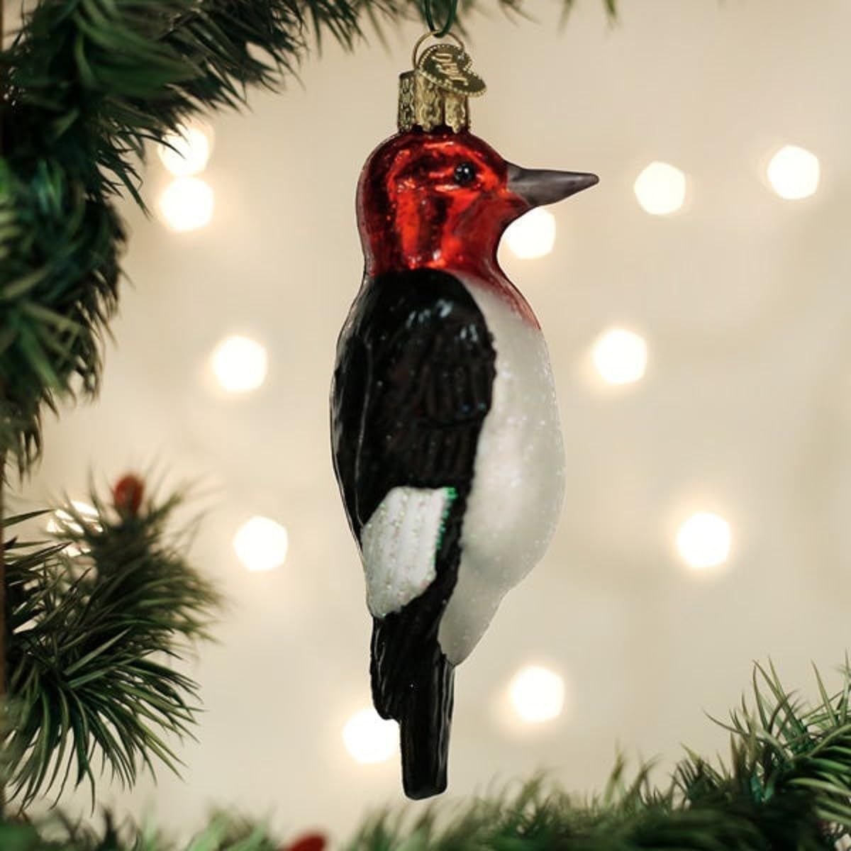 Positions the product as a Christmas ornament by showing it hanging on a tree with holiday lights and greenery, communicating its seasonal gifting and decorative purpose.