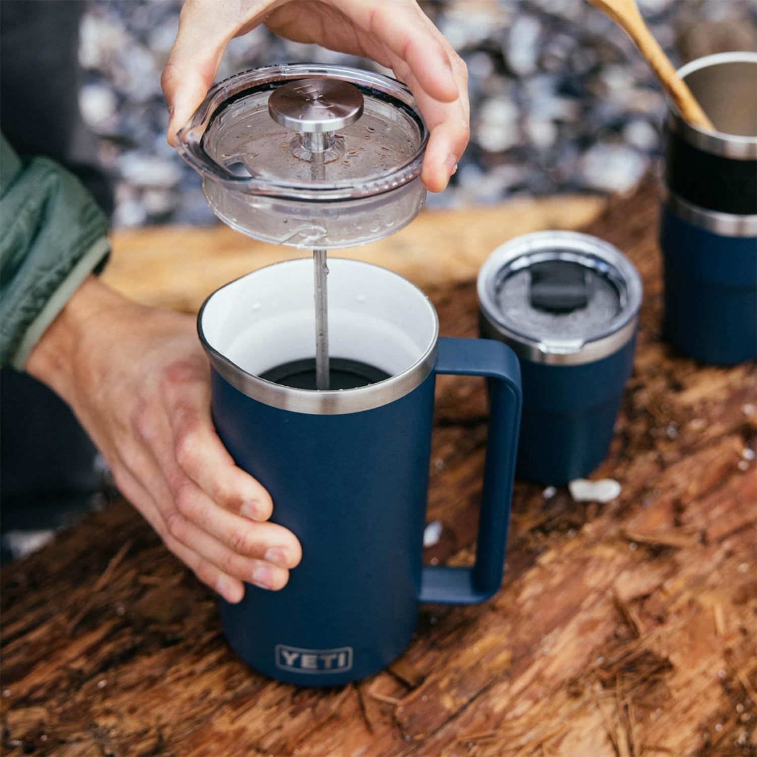 Shows the coffee press being used in a real outdoor setting to help shoppers visualize the product in use during camping or outdoor activities.