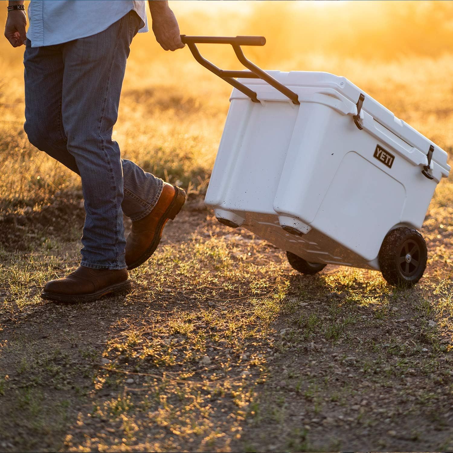 Depicts the cooler being pulled by a person in an outdoor field setting at sunset, showing real-world portability and ease of transport without any text or callouts.