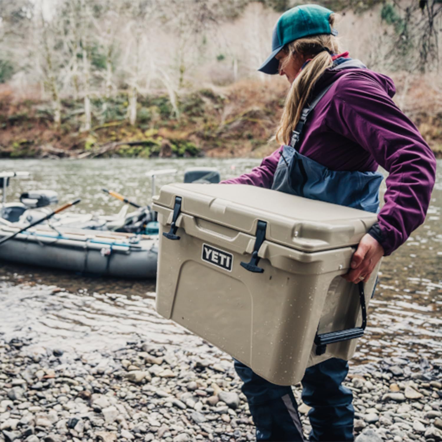 Demonstrates the cooler in a real-world outdoor setting with a person carrying it by a river, showing its portability and rugged use context without any text overlay.