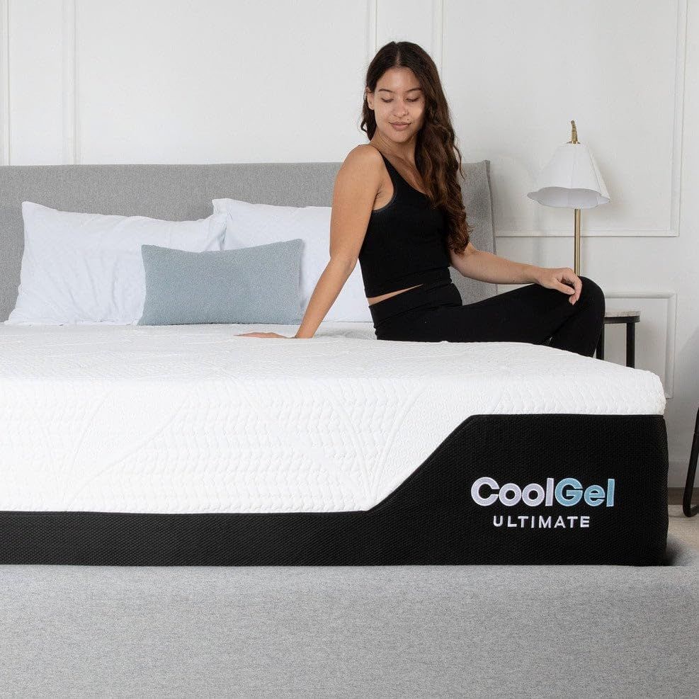Displays the mattress in a real bedroom environment with a person sitting on it, helping shoppers visualize the product in their own home.