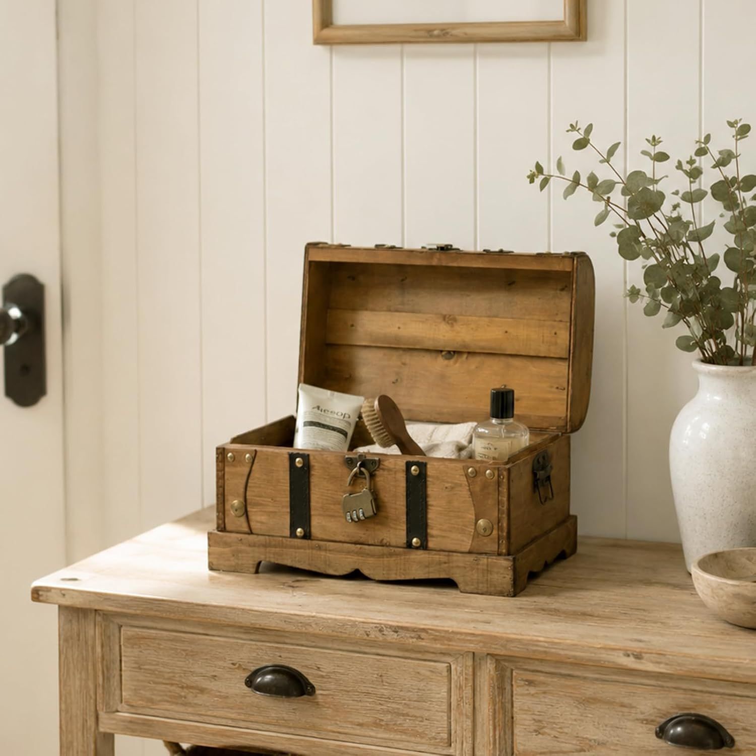 Shows the trunk styled in a home setting holding bath items, conveying its use as a decorative storage piece.