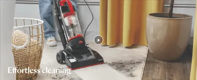 Shows the vacuum cleaning a rug in a real home setting to convey easy, effective cleaning, with a video for more detail.