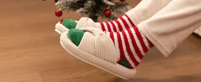 Positions the slippers as a cozy holiday gift by showing them worn near a decorated Christmas tree. Shows the slippers being worn in a real home setting with no text overlay to build an…