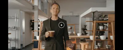 Shows a real person enjoying RYZE coffee in an everyday setting to make the product feel relatable and aspirational.