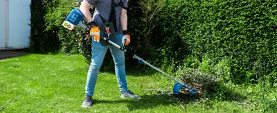 Lifestyle photo of the trimmer in use gives shoppers a sense of its scale and handling in a real yard setting.