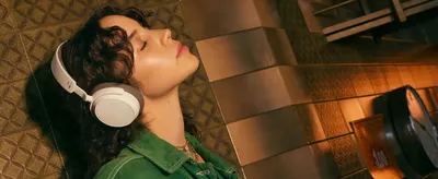 Shows a model relaxing with the headphones in a warm urban setting to help shoppers picture everyday listening.