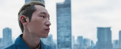 Shows a man wearing the earbud in a city setting so shoppers can picture everyday use.