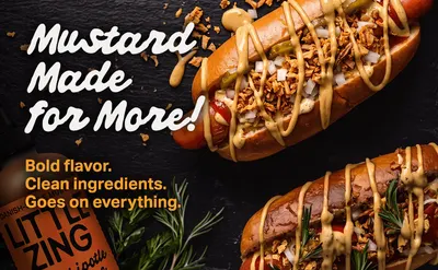 Shows the mustard drizzled on gourmet hot dogs in a styled food scene to help shoppers envision using it on everyday meals. Headline Mustard Made for More and the copy Bold flavor Clean ingredients…