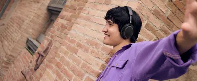 Shows a smiling young man wearing the headphones in a city setting to help shoppers picture enjoying music on the go.