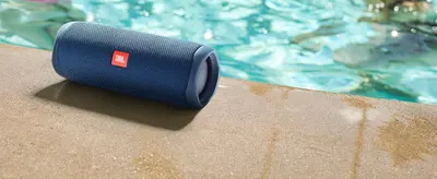 Shows the speaker resting poolside in a relaxed outdoor setting to help shoppers envision using it at the pool or beach. No text overlay so the scene speaks for itself.