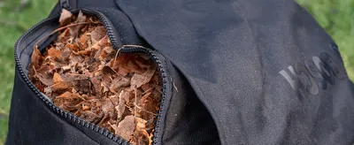 Shows the product bag filled with leaves in a natural garden setting to help shoppers picture the collection capacity in real use.