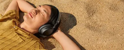 Shows a relaxed listener on sand with the headphones to help shoppers imagine casual, carefree use.