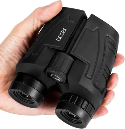 Shows the binoculars held in hand to demonstrate their compact, portable size and ergonomic design for easy carrying and use. Uses a human hand to provide scale reference and demonstrate how the…