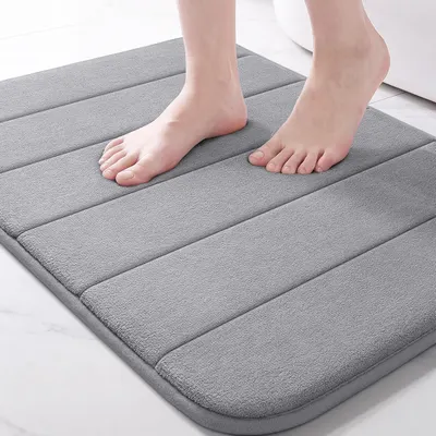 Shows the bath mat in use with feet standing on it to demonstrate its soft, cushioned comfort and plush texture, reassuring shoppers of its quality and comfort. Uses a person's feet to provide scale…