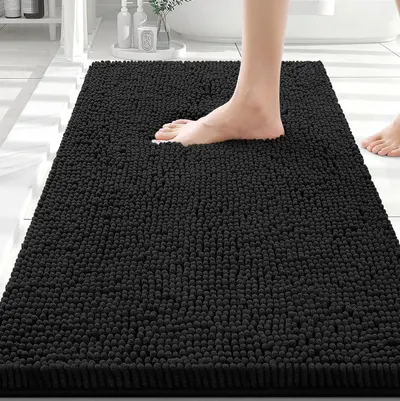 Shows a person standing on the bath mat to demonstrate its size, plush texture, and comfort underfoot, helping shoppers visualize how it will feel and fit in their bathroom. Displays the bath mat in…