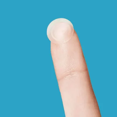 Demonstrates the extremely small size of the product, likely a contact lens or similar item, by showing it on a fingertip.