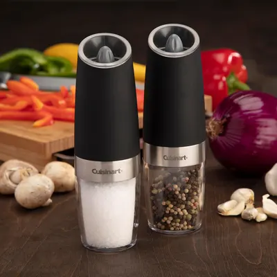 Shows the salt and pepper grinders in a real kitchen setting, surrounded by fresh ingredients, to demonstrate their practical use in food preparation.