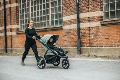 Shows the stroller being used in a real-world urban setting, demonstrating its practicality for daily life and city navigation.
